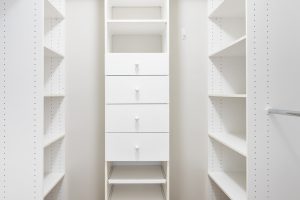 Photo of an empty walk in closet with white shelves, drawers and wall.